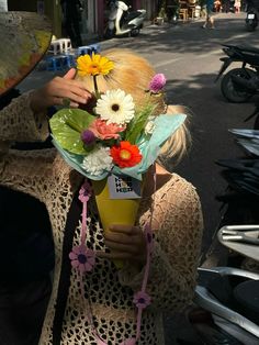 a woman holding a bouquet of flowers in her hands while standing on the side of a road