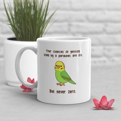 a green bird sitting on top of a white coffee mug next to a pink flower