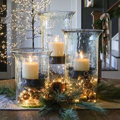 three glass vases filled with lit candles on top of a table next to christmas decorations