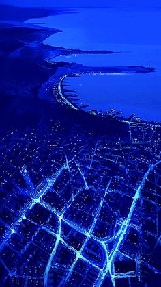 an aerial view of a city at night with lights on the streets and water in the background