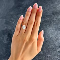 a woman's hand with a diamond ring on her left hand, against a gray background