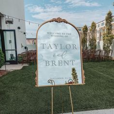 a sign that is sitting in the grass near some chairs and tables with flowers on them