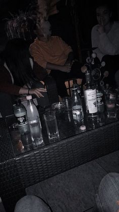 people sitting at a table with bottles and glasses on it