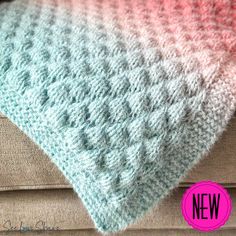 a crocheted blanket sitting on top of a couch next to a pink and blue pillow