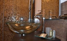 a glass bowl sink sitting on top of a wooden counter next to a mirror and soap dispenser