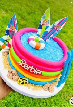 someone holding up a cake decorated with surfboards and inflatable rafts on the grass