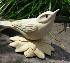 a white bird statue sitting on top of a rock next to green plants and grass