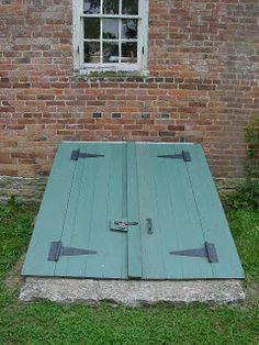 an old wooden door sitting in front of a brick building with grass and bushes around it