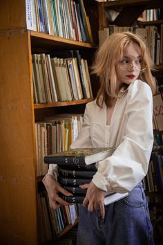 a woman holding a stack of books in front of a book shelf