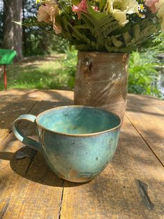 a blue cup sitting on top of a wooden table next to a vase filled with flowers