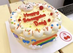 a happy birthday cake with white frosting and rainbow decorations on top, sitting on a table