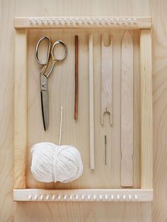 yarn, scissors and knitting needles are in a wooden box on a shelf with pegs