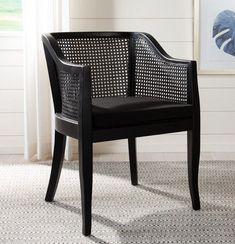 a black chair with wicker back and arm rests against a wall in front of a window