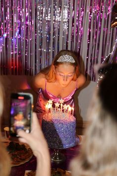 a woman holding a cake with lit candles on it in front of a phone and some other people