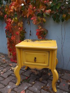 a yellow table sitting on top of a brick floor next to a wall covered in leaves