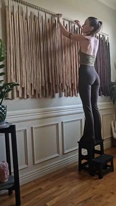 a woman standing on top of a stool in front of a wall with curtains behind her