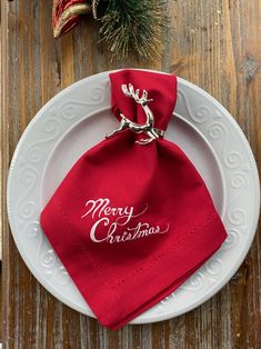 a white plate topped with a red napkin on top of a wooden table next to a christmas tree