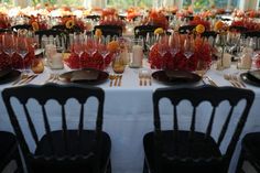 a long table is set with black chairs and white tablescloths, orange centerpieces and candles