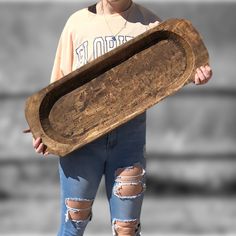 a woman holding a wooden tray with holes on it's sides and wearing ripped jeans