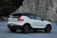 a white volvo suv parked in front of a rocky cliff face with black rims