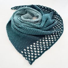 a knitted scarf on a white surface with blue and green colors, in the shape of a triangle