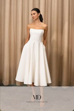 a woman standing in front of a curtain wearing a white strapless dress and high heels