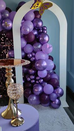 purple balloons are on display in front of a large arch and table with a cake