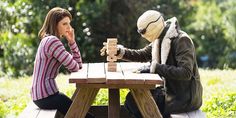 two people are sitting at a picnic table playing chess with an animal statue in the background