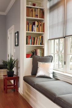 a window seat with bookshelves behind it and a potted plant in the corner