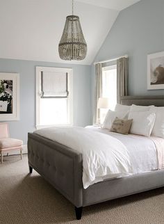 a bedroom with blue walls, white bedding and a chandelier hanging from the ceiling