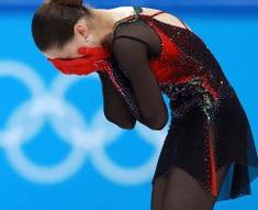 a female figure skating on the ice in an olympic event with her hands behind her head