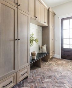 an entryway with built in cabinets and a bench on the brick floor, along with a potted plant