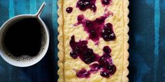 a pastry with blueberries on it next to a cup of coffee and spoons