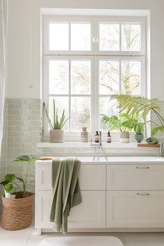 a white kitchen with green plants in the window sill and towels on the counter