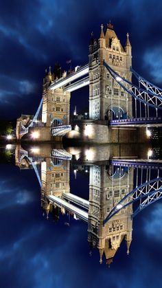 the tower bridge is lit up at night with its lights on and reflecting in the water