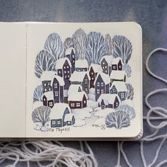 an open book with a drawing of houses and trees in the snow on top of it