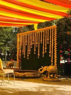 an outdoor area with yellow and orange decorations on the walls, chairs and tables under a canopy