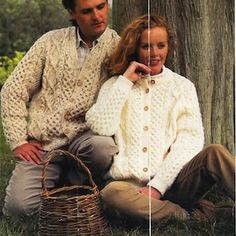 a man and woman sitting next to each other in front of a tree wearing sweaters