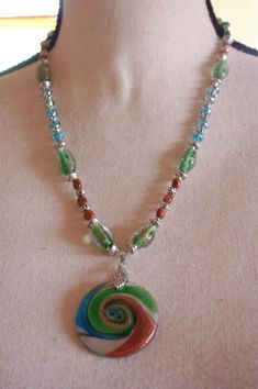 I designed and hand crafted this lovely hand beaded pendant necklace.  It has a beautiful lampworked glass pendant, and lampworked glass, natural stone, glass, and silver metallic beads.    The lampworked glass pendant and beads have a bit of sparkle - for just a touch of bling!  The colors are green, turquoise, bronze, silver, and clear/white.   This unique necklace measures 21 inches in length, and the pendant adds an additional 2.25 Inches.  It has a J-hook clasp, and is comfortable to wear. Ours is a non-smoking home. Recycled Glass Round Beads Jewelry For Gifts, Recycled Glass Round Beads Jewelry Gift, Spiral Multicolor Necklace Gift, Multicolor Spiral Necklace Gift, Recycled Glass Beaded Necklaces With Round Beads As Gift, Recycled Glass Beaded Necklaces As Gifts, Recycled Glass Beaded Necklaces For Gifts, Recycled Glass Beaded Necklace With Round Beads As Gift, Unique Glass Pendant Necklaces