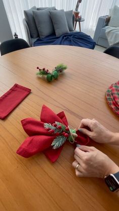 someone is making a christmas bow on a table with red napkins and greenery