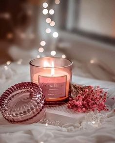 a pink candle sitting on top of a bed next to a glass bowl filled with flowers