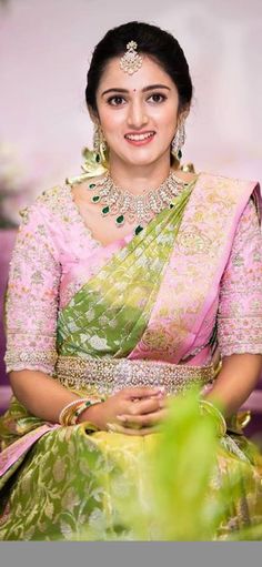 a woman in a green and pink sari sitting on a purple couch with greenery