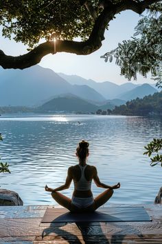 a woman is sitting in the middle of a yoga pose on a dock overlooking a body of water