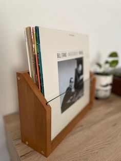 a wooden shelf with books and magazines in it on top of a wood table next to a potted plant