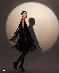 a woman standing in front of a white ball with her shadow on the wall behind her