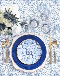 a blue and white place setting with silverware, flowers and napkins on the table