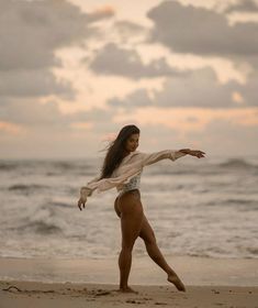 a woman is standing on the beach with her arms outstretched