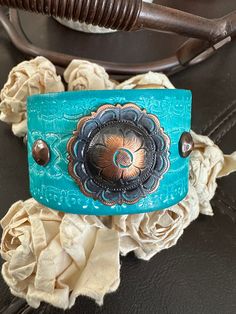 bracelet cuff, western jewelry  Genuine white distressed embossed leather strap has been given a turquoise dye and adorned with an antiqued copper flower concho.  The cuff is accented with four copper rivets and one copper snap has been placed to fit up to a 6 3/4" wrist. ✨I CAN ADD ANOTHER SNAP IF YOU WOULD LIKE A SMALLER OR LARGER SIZE BUT YOU NEED TO MESSAGE ME BEFORE PURCHASING  The last photo features other items available for purchase in my shop and not included in this listing As with all patina surfaces, color could transfer so extra care should be taken to avoid dye transfer- it is not water proof  other cuffs available https://www.etsy.com/shop/AsYouWishgallery?ref=seller-platform-mcnav§ion_id=18358191 I can also design this using vegan leather. If interested, just convo me and I Adjustable Western Cuff Bracelet For Festivals, Adjustable Western Style Cuff Bracelet For Festivals, Western Style Adjustable Cuff Bracelet For Festivals, Adjustable Western Style Festival Cuff Bracelet, Southwestern Concho Cuff Bracelet For Festivals, Western Concho Bracelets For Festival, Western Style Concho Bracelets For Festivals, Handmade Western Style Turquoise Bracelet, Handmade Western Turquoise Bracelets