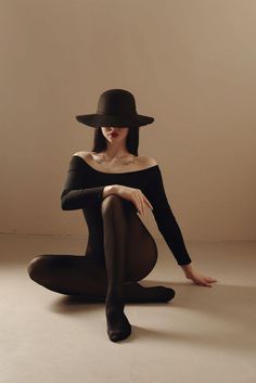 a woman in black is sitting on the floor with her legs crossed and wearing a hat