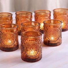 there are many glass cups that have candles in them on the table next to each other